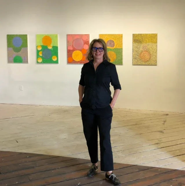 Woman in black outfit standing in art gallery with colorful abstract paintings on the wall.